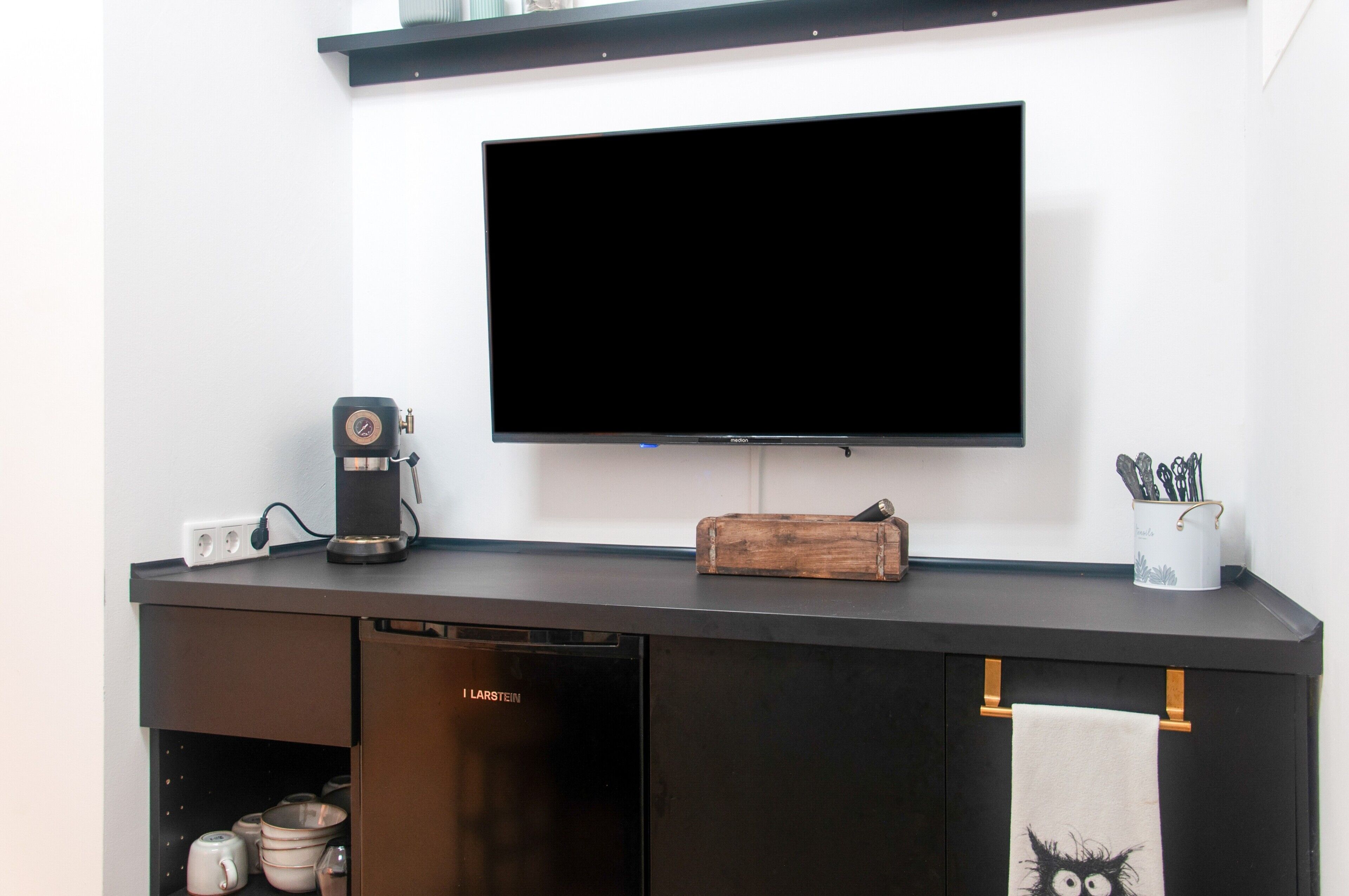 Eine moderne Küche mit einem Flachbildfernseher, der über einer schwarzen Arbeitsplatte angebracht ist.