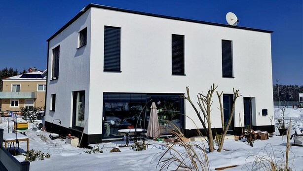A modern two-story house with a garage, surrounded by snow.