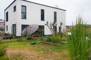 A modern two-story building with a flat roof, satellite dish, and a garden area with plants and outdoor furniture. - Apartment 'Süße Kleine Keller' with Wi-Fi (Hagenbüchach)