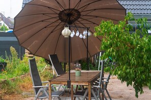 An outdoor patio with a table and chairs, an umbrella, and a hanging light fixture. - Apartment 'Süße Kleine Keller' with Wi-Fi (Hagenbüchach)