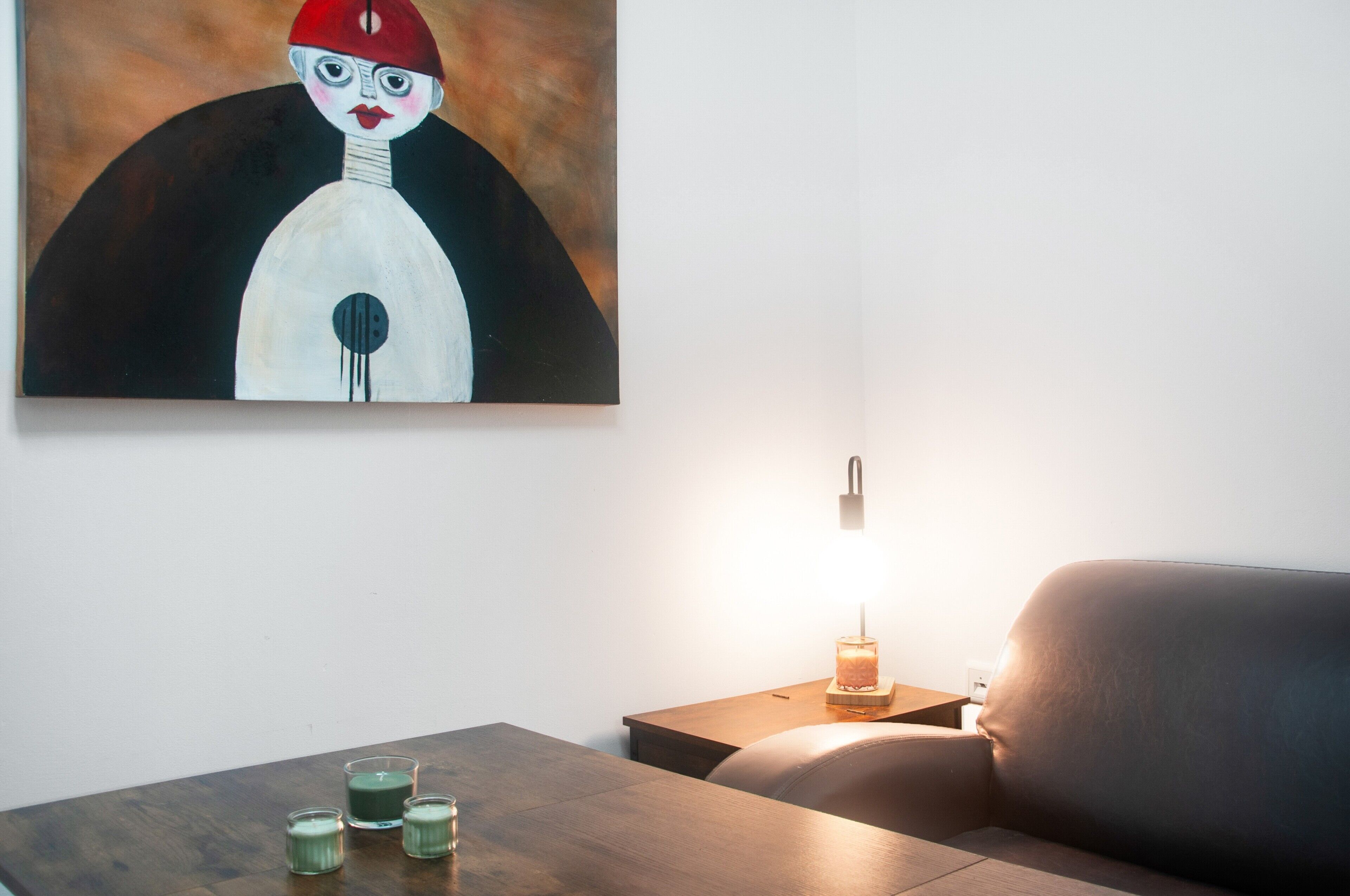 Et værelse med et maleri på væggen, et bord med stearinlys og en lampe på et sengebord.