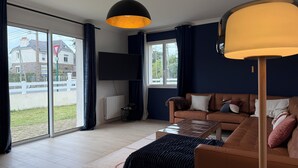 Una sala de estar con un sofá, una mesa de centro, un televisor montado en la pared y un ventanal con cortinas.