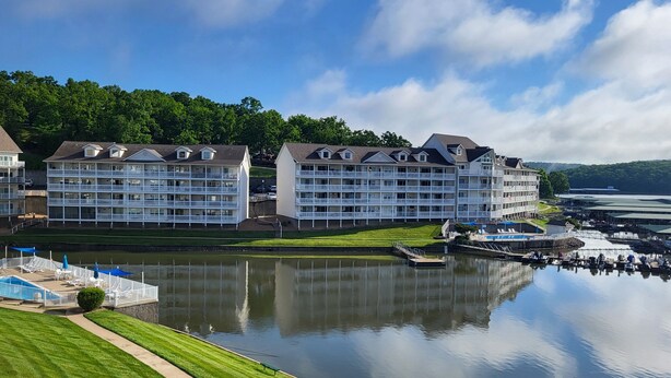 Ein Hotel am Wasserufer mit mehreren Balkonen, einer Anlegestelle und einem Spiegelbild im Wasser.