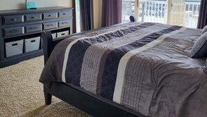 Ein Schlafzimmer mit Bett, Deckenventilator, Fernseher, Kommode und Blick auf eine Brücke und Grünflächen.