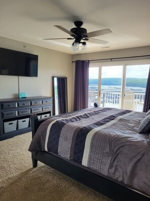 Ein Schlafzimmer mit Bett, Deckenventilator, Fernseher, Kommode und Blick auf eine Brücke und Grünflächen.