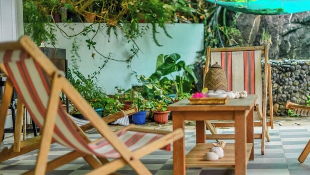Un espace extérieur aménagé avec des meubles en bois, comprenant des chaises et une table, entouré de plantes en pot et d’un mur en pierre.