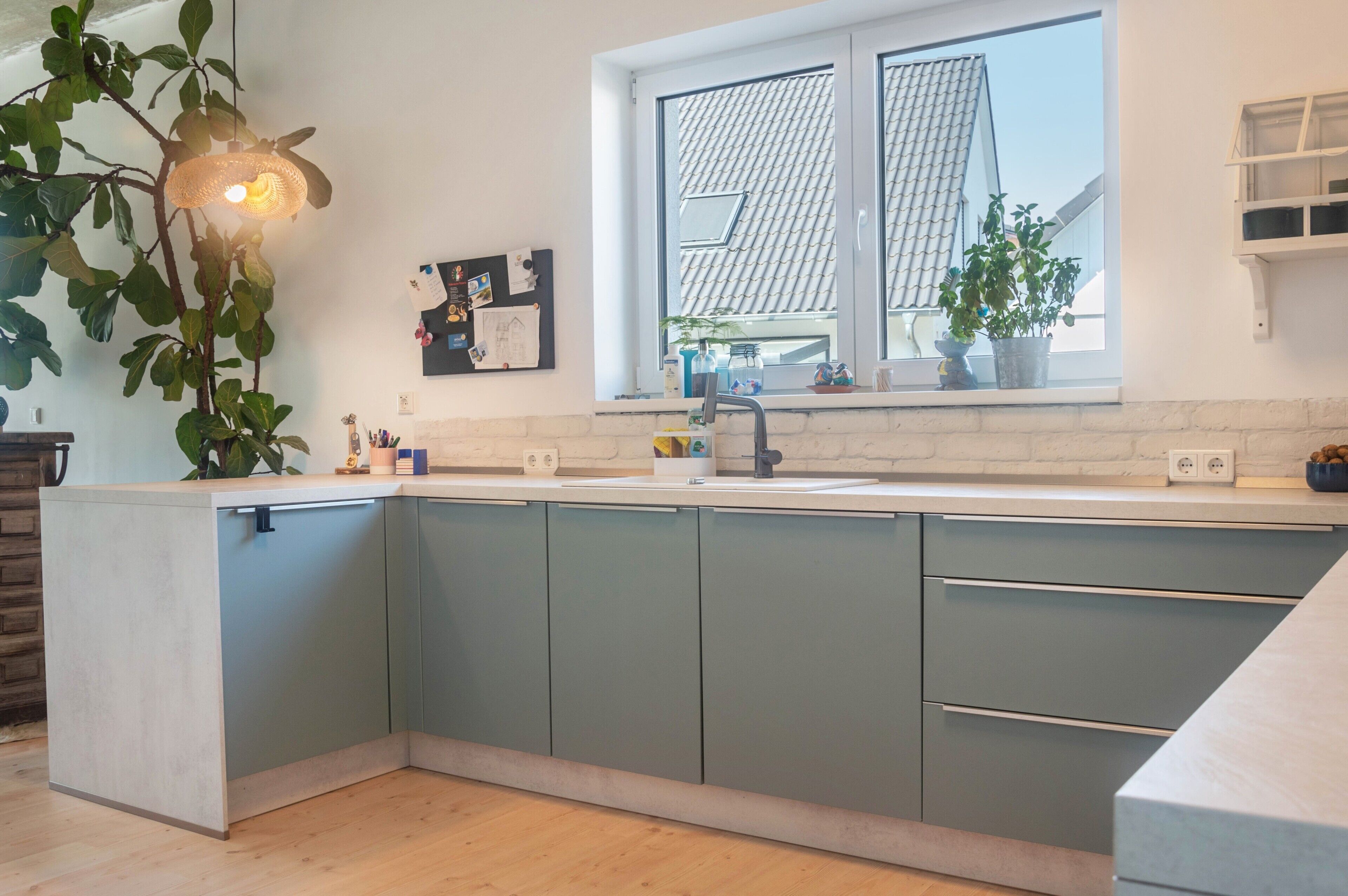 Una cocina con ventana, armarios, un lavamanos y una lámpara colgante.