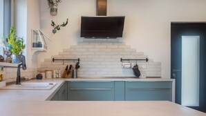 Una cocina moderna con televisor de pantalla plana, salpicadero de ladrillo blanco, gabinetes azules y una ventana con plantas.