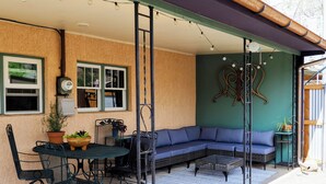 Eine überdachte Terrasse mit Esstisch und Stühlen, einem blauen Sofa und einem dekorativen Wandbild.