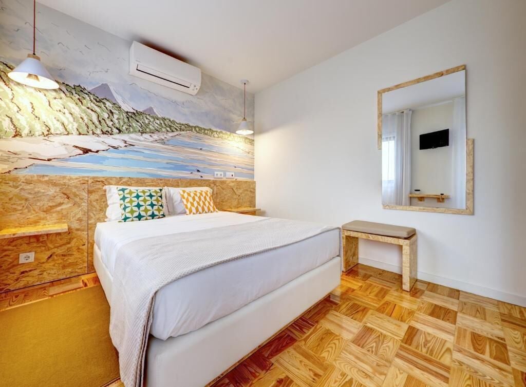 A bedroom with a bed, a bedside table, a wall-mounted TV, and a wooden floor.