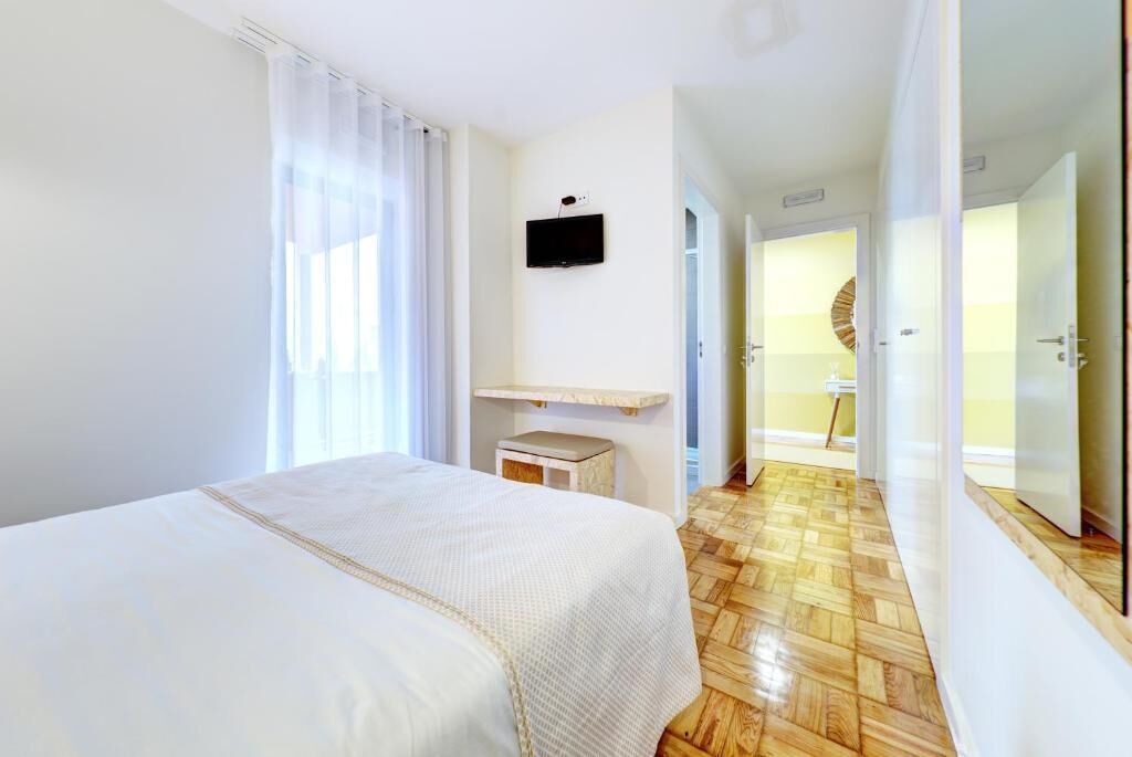 A hotel room with a bed, a television, a small stool, and a wooden floor.