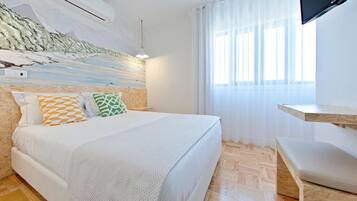Un dormitorio con cama, televisión, ventana con cortinas y aire acondicionado instalado en la pared.