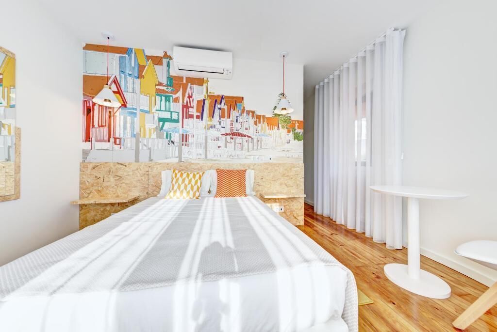 A hotel room with a bed, a wall mural, a white table, and a white chair.