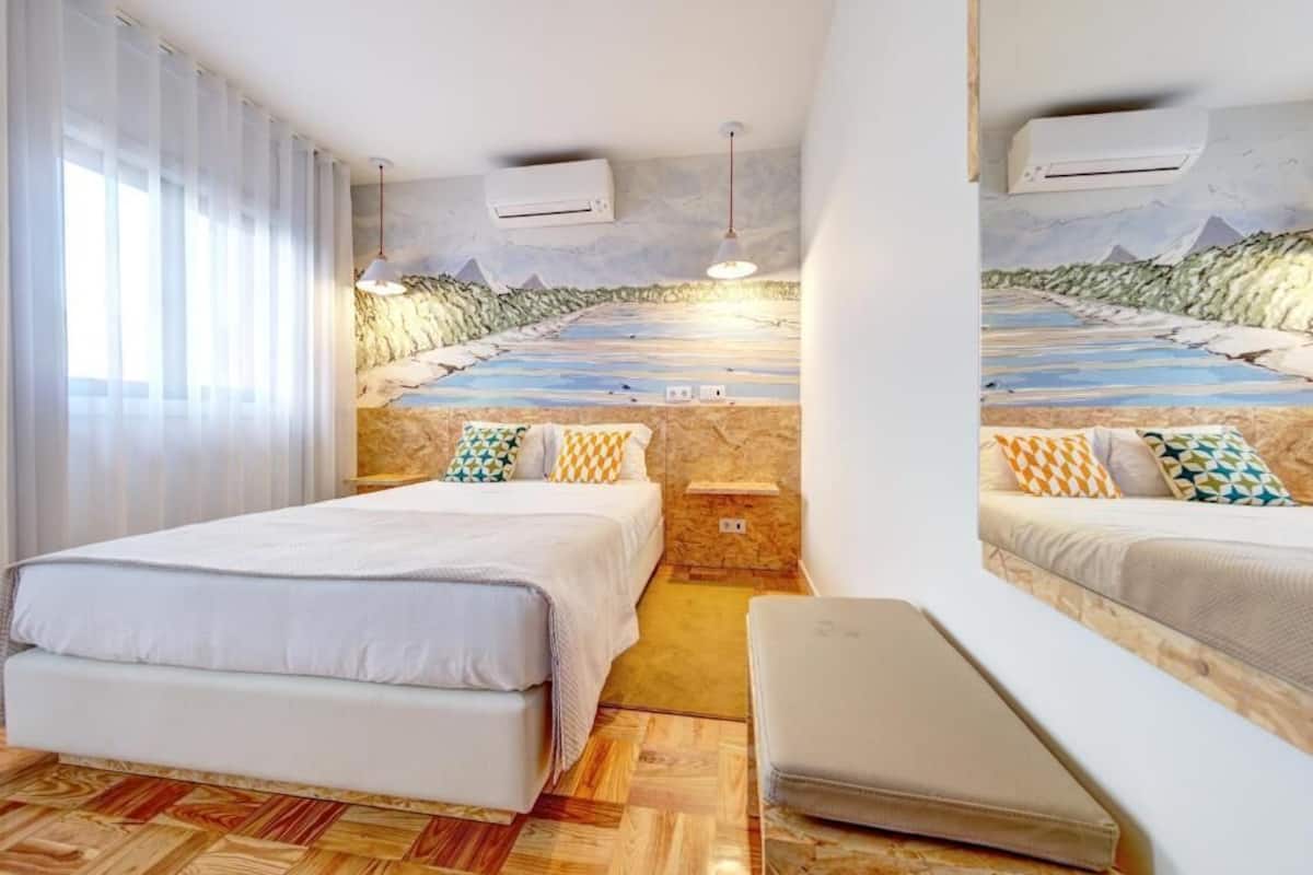 A hotel room with two beds, a stone wall, an air conditioning unit, and a mural of a landscape.