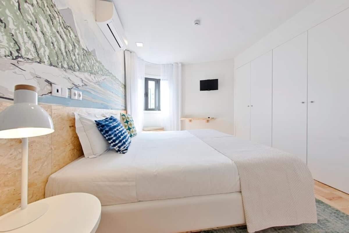 A bedroom with a bed, bedside table, lamp, and a wall-mounted TV.