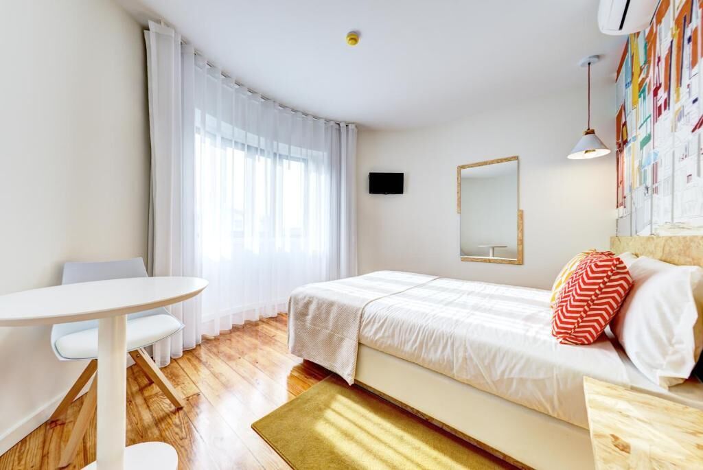 A bedroom with a bed, a desk, a chair, a television, and a mirror.