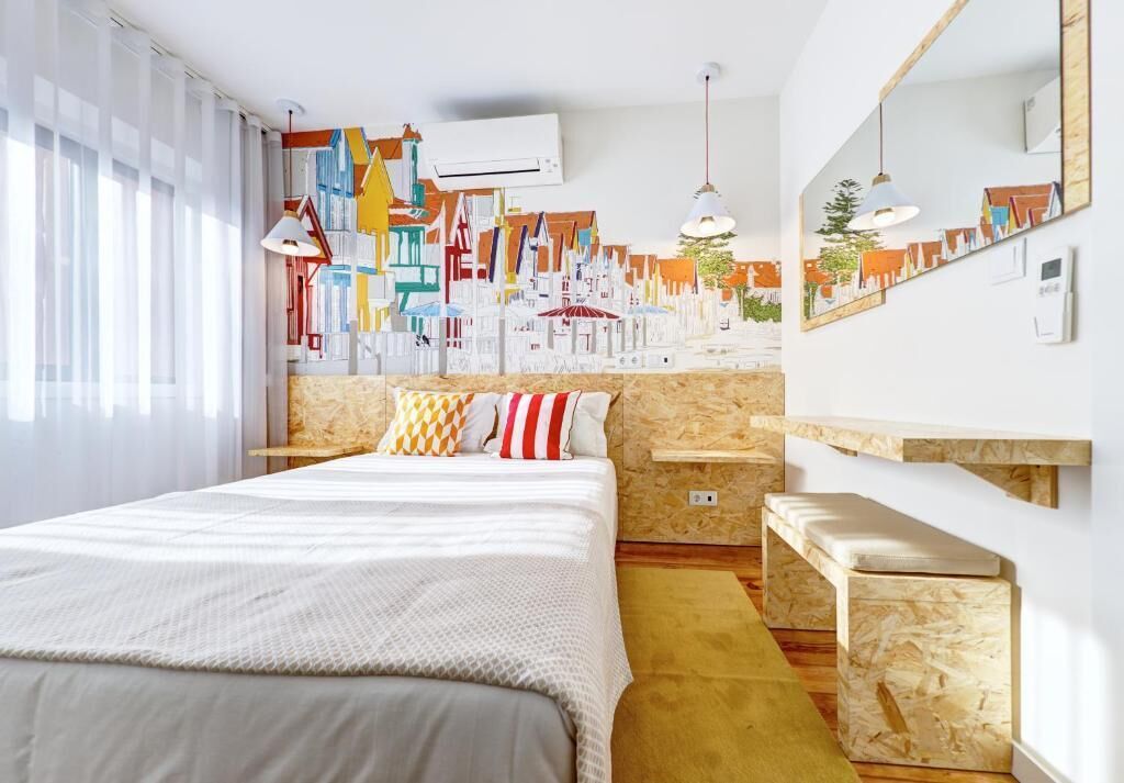 Habitación de hotel moderna con una cama grande, un cabecero de madera, un pequeño banco y un mural de un paisaje urbano colorido en la pared.