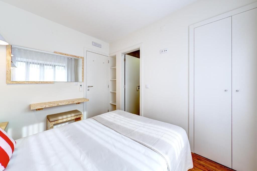 A bedroom with a bed, a bedside table, a mirror, a wardrobe, and a door leading to another room.