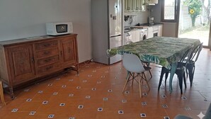 A compact kitchen with a microwave, refrigerator, and washing machine. A dining table with chairs is positioned in the center. - House by the sea in the most beautiful village of Asturias!!! (Muros de Nalón)