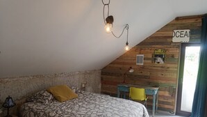 A bedroom with a sloped ceiling, a bed with patterned bedding, a desk with a chair, and a sign on the wall. - House by the sea in the most beautiful village of Asturias!!! (Muros de Nalón)