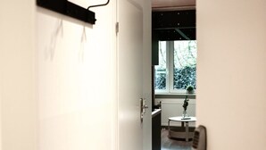 Un couloir menant à une cuisine avec une fenêtre, un radiateur et une plante posée sur le rebord de la fenêtre.