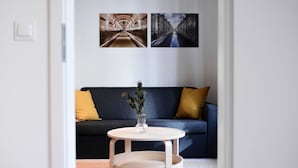 Een kamer met een donkerblauwe bank, een witte ronde tafel met een vaas, en twee aan de muur bevestigde afbeeldingen.