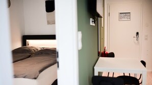 Een slaapkamer met een bed, nachtkastje, stoel en een deur met een brandblusser.