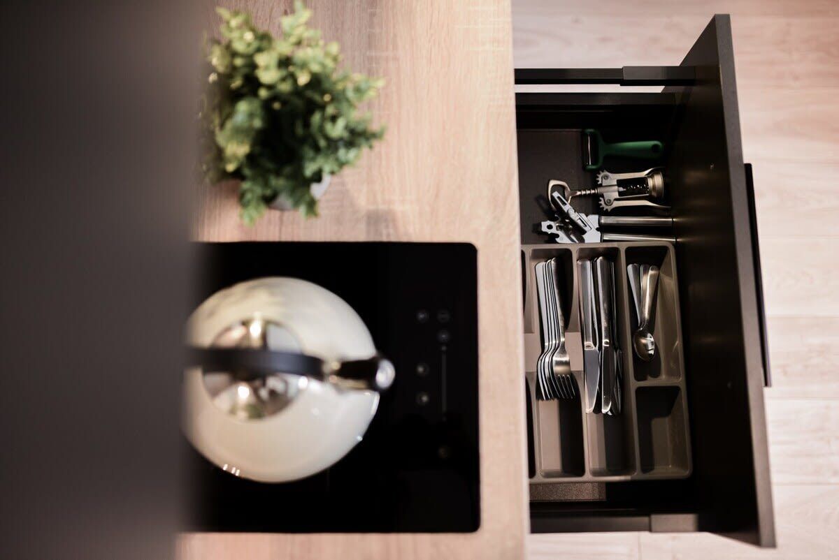 Une cuisine équipée d’appareils électroménagers intégrés, agrémentée d’une plante et dotée d’un rangement pour les ustensiles.