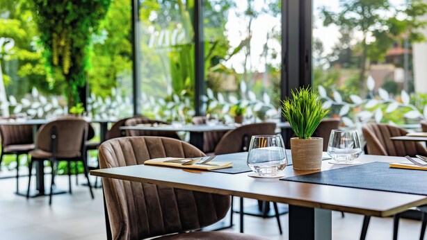 A restaurant with tables set for dining, chairs, and a potted plant on the table. - Park Hotel (Mosonmagyaróvár)
