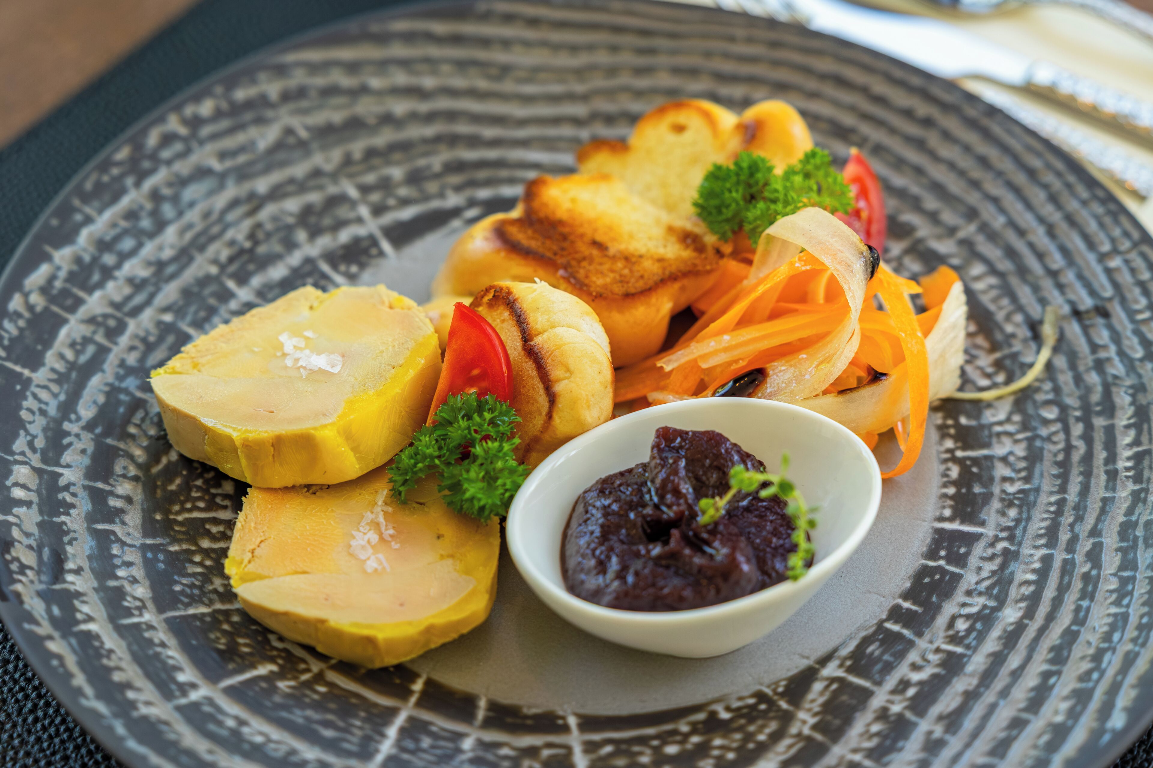 Un plato con fruta amarilla en rodajas, verduras a la parrilla y un recipiente pequeño con salsa oscura.