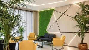 A modern interior with a green wall, yellow chairs, a black sofa, and potted plants. - Park Hotel (Mosonmagyaróvár)