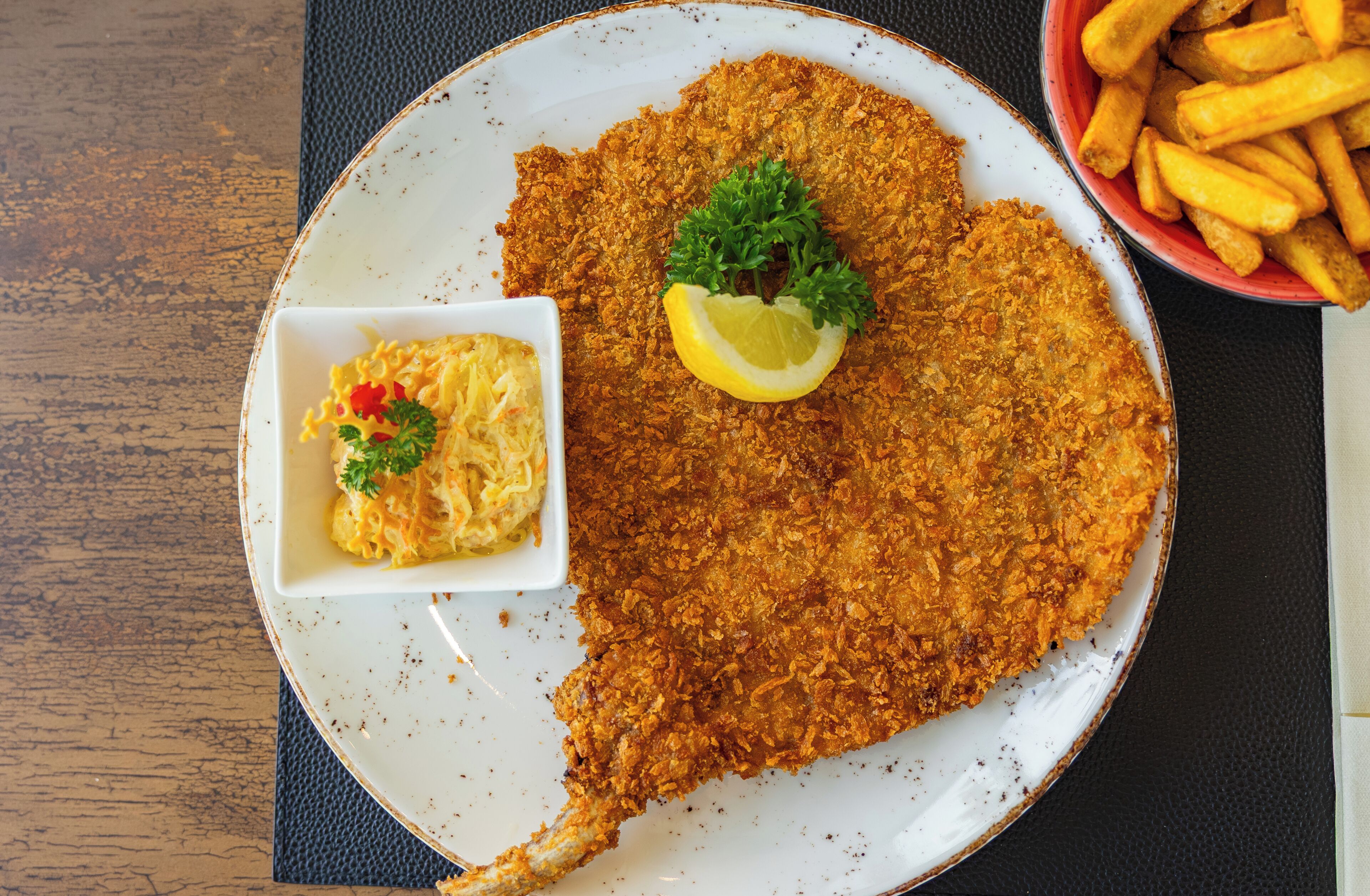 Un plato con milanesa, papas fritas y una ensalada de macarrones.