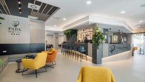 A modern hotel lobby with a reception desk, bar area, seating, and a large plant. - Park Hotel (Mosonmagyaróvár)