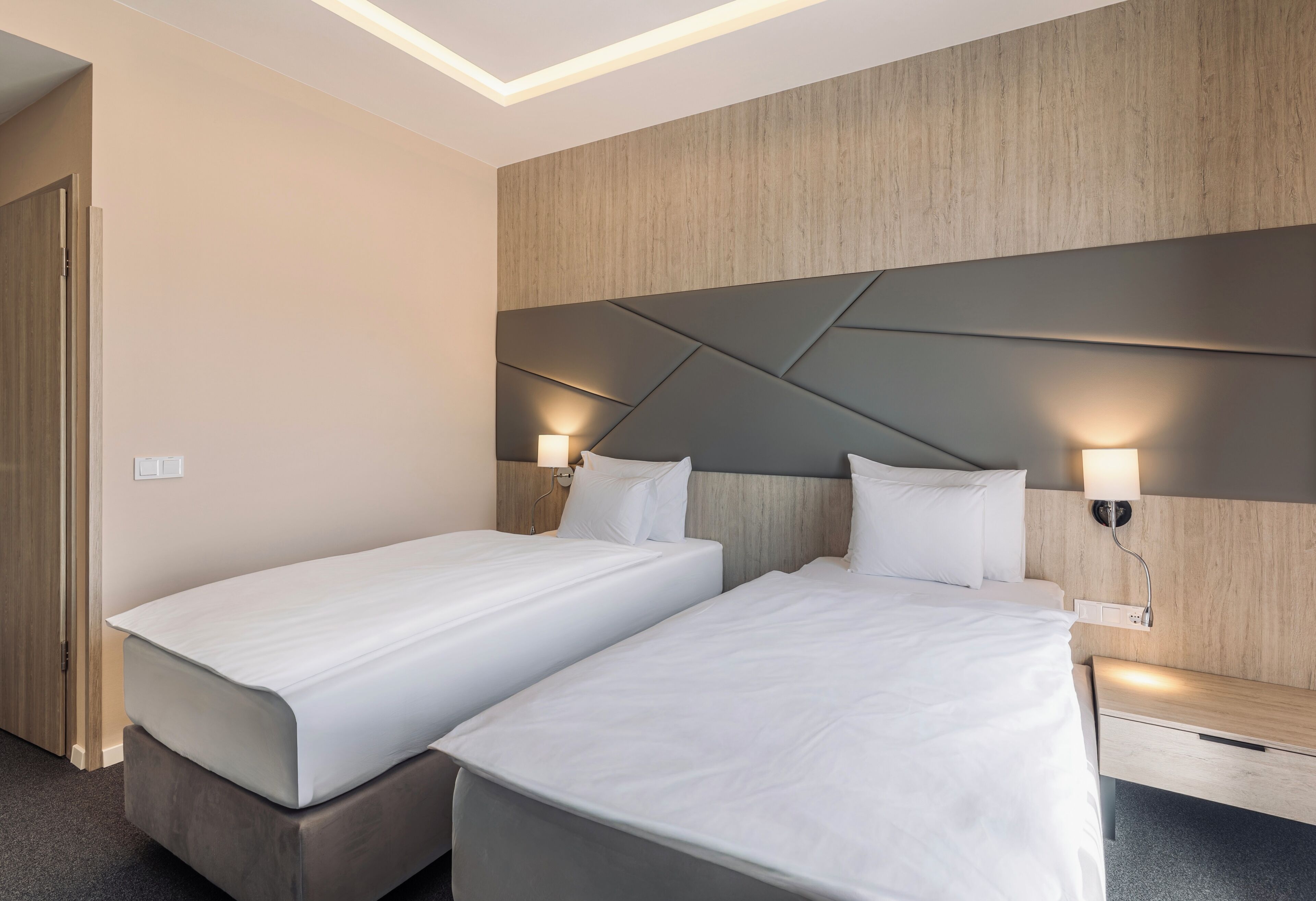 A hotel room with two beds, a wooden headboard, bedside lamps, and a built-in bench.