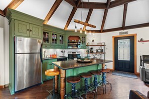 A kitchen with green cabinets, a stainless steel refrigerator, a wooden island with stools, and a black door with a ski-themed sign. - New Listing! Lakeside Retreat | Fire Pit | Deck with Lake View (Blanchard)