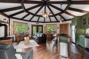 A rustic cabin interior with a wooden ceiling, a fireplace, a sofa, a dining area, and green cabinets. - New Listing! Lakeside Retreat | Fire Pit | Deck with Lake View (Blanchard)