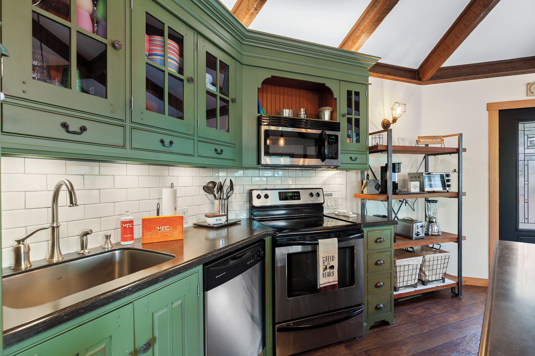 A kitchen with green cabinets, a stainless steel dishwasher, a black oven, and a microwave.