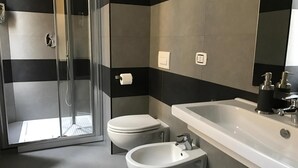 Un baño moderno con cabina de ducha de vidrio, inodoro, bidé y un lavabo grande con espejo.