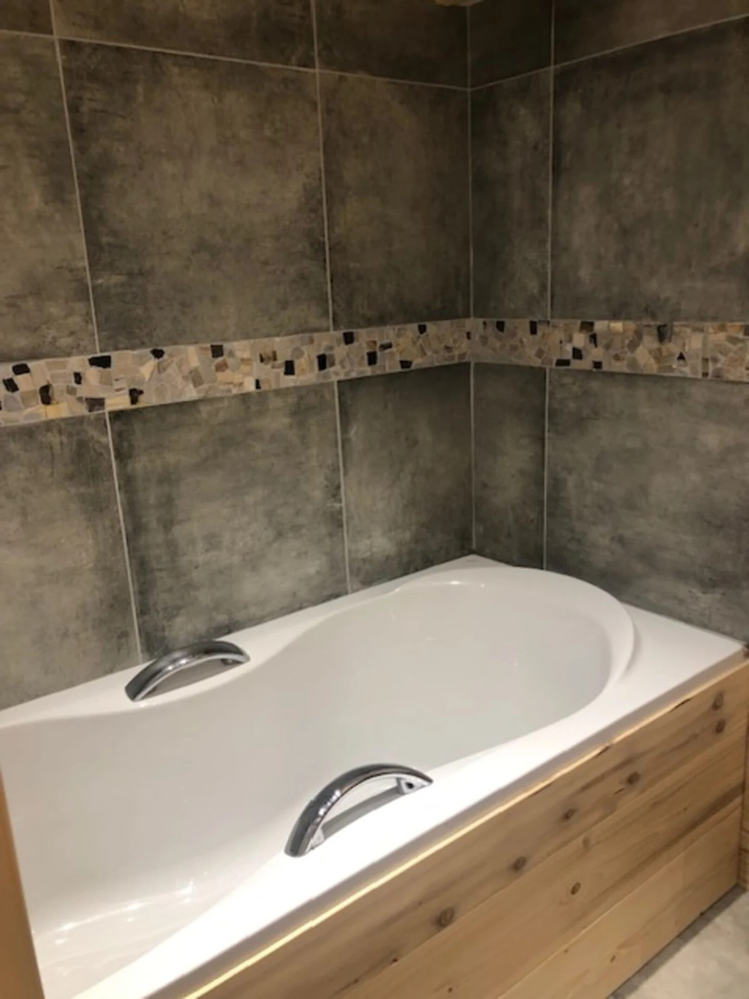 A bathroom with a freestanding bathtub, wooden cabinetry, and tiled walls.