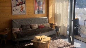 A cozy room with a sofa, a wooden coffee table, and a glass door leading to a snowy outdoor area. - Apartment “Les Gentianes” Valley & Mountain View, 6 Guests, 3 Bedrooms (Chamrousse)