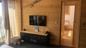 A wooden-paneled room with a flat-screen TV mounted on the wall, a small console table with decorative items, and a door leading to another room. - Apartment “Les Gentianes” Valley & Mountain View, 6 Guests, 3 Bedrooms (Chamrousse)