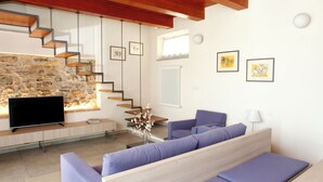 Una sala de estar moderna con una pared de piedra, un televisor de pantalla plana, un sofá y una escalera.