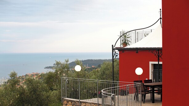 Un balcón con un muro de piedra, un edificio rojo y vista al mar.