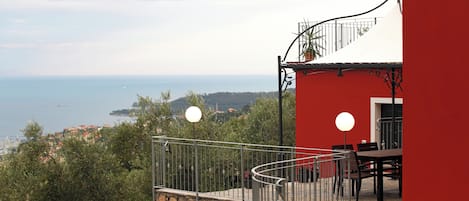 A balcony with a stone wall, a red building, and a view of the sea.