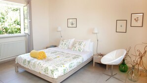 Un dormitorio con cama, mesitas de noche, una silla e imágenes enmarcadas en la pared.