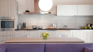 Una cocina moderna con horno empotrado, campana extractora de acero inoxidable y un bol con manzanas verdes en la encimera.