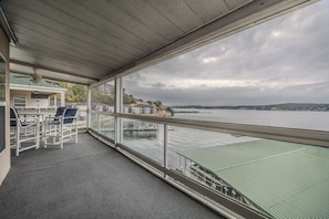 Ein Balkon mit Blick auf ein Gewässer, ein überdachter Bereich mit Stühlen und ein Gebäude im Hintergrund.