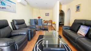 Ein Wohnzimmer mit zwei schwarzen Ledersofas, einem Glastisch und einem Essbereich mit Tisch und Stühlen.