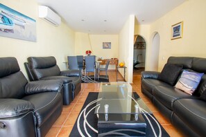 Ein Wohnzimmer mit zwei schwarzen Ledersofas, einem Glastisch und einem Essbereich mit Tisch und Stühlen.