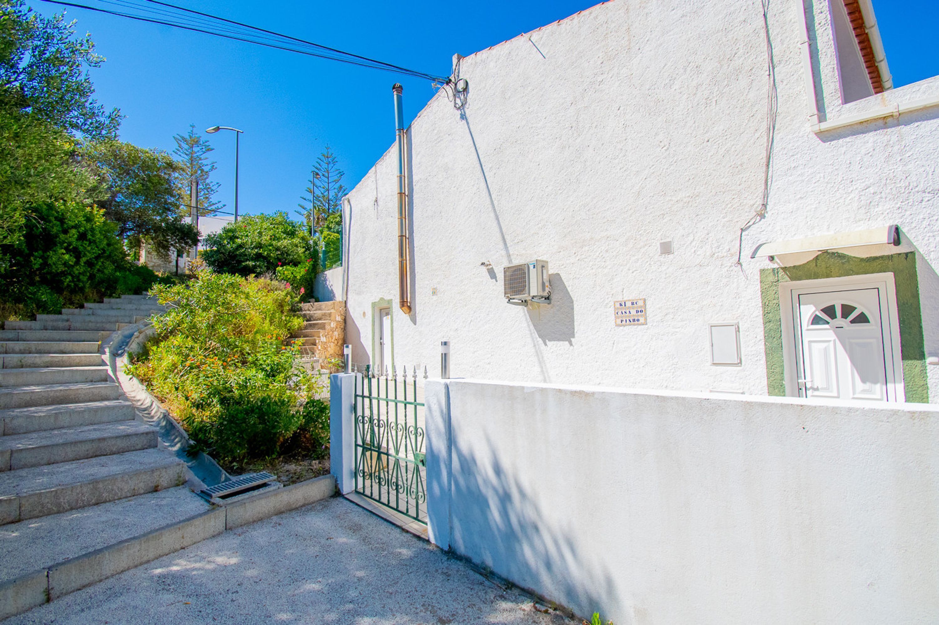 Un bâtiment blanc avec un escalier menant à l’étage, une porte en métal et une petite porte d’entrée.